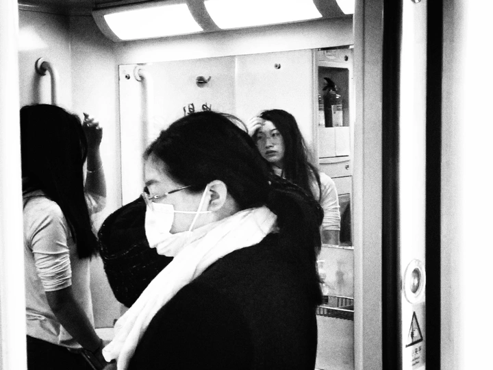 一名戴着手套的女子站在地铁列车内 另一名女子正在看手机。