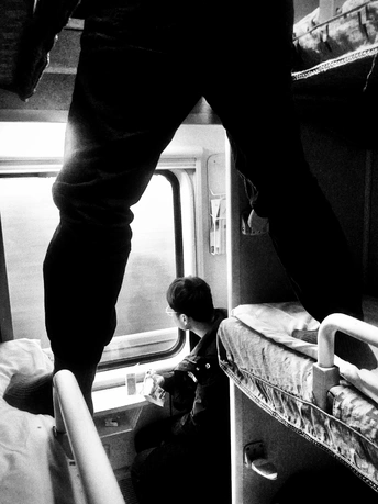 一张黑白照片 一个人坐在火车上 脚边有行李。