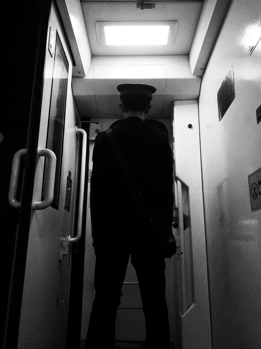 一个穿西装戴帽子的男人站在一个通往光线昏暗的房间的走廊里