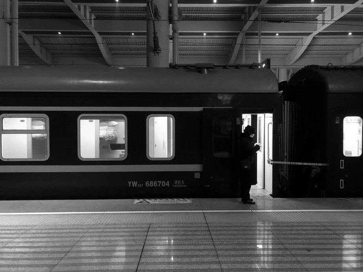 一张黑白照片 背景是火车站 一个人站在站台上 火车在背景中。