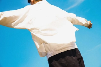 一个穿白衬衫的年轻人张开双臂 看着一只风筝在蔚蓝的天空中飞翔。