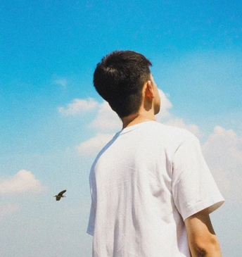 一位穿着白衬衫的年轻人正在看一只风筝在蓝天中飞翔。