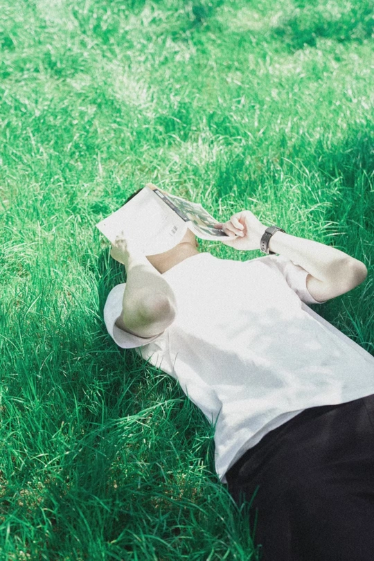 一个年轻女子躺在绿草地上读书