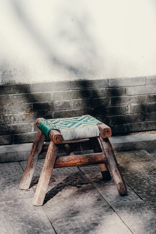 一个带有靠垫的小木凳坐在砖墙前。