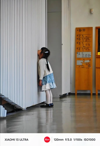 一个小孩子站在一条走廊里 正看着墙上顶着他们头的小人。