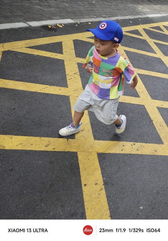 一个戴帽子的年轻男孩走过停车场的一条街道 而另一个小男孩走过马路。