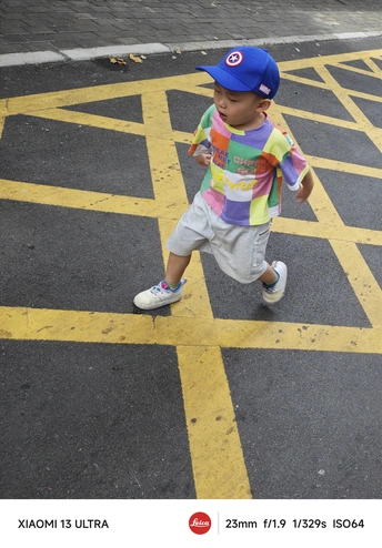 一个戴帽子的年轻男孩走过停车场的一条街道 而另一个小男孩走过马路。