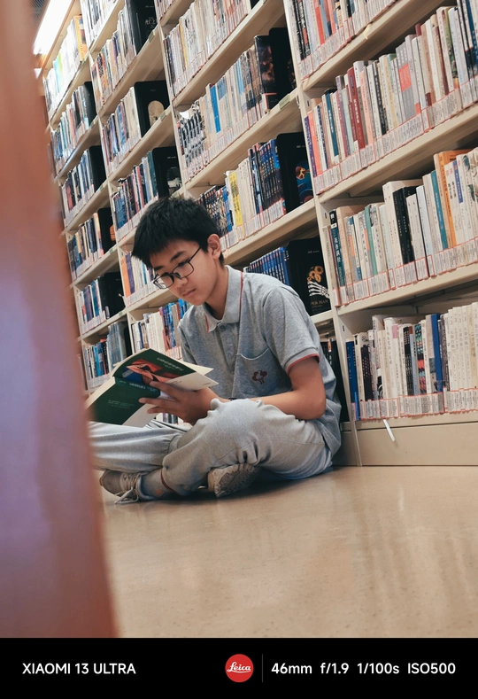 一个戴眼镜的男孩坐在图书馆地板上阅读一本书