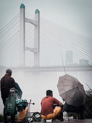 几位男士坐在自行车上 带着雨伞 在雨中 背景是一座桥 前景是一条河 河上有人们。