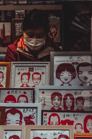 一个戴红面具的人走过一家出售人脸肖像的商店。