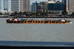 一艘黄色船在大片水域中 背景是高耸的建筑物。