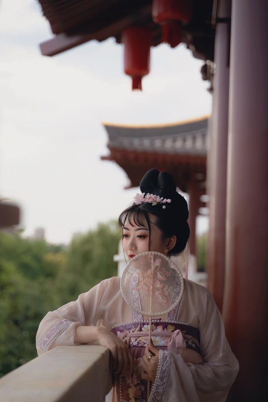 一位穿着和服的年轻女子手持扇子和雨伞站在墙上