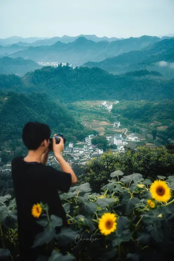 站在山丘上的男子正在给山谷拍照 山谷里有向日葵和远处的城市。