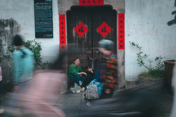 一个男子骑自行车经过一栋建筑旁 门上坐着个男孩。