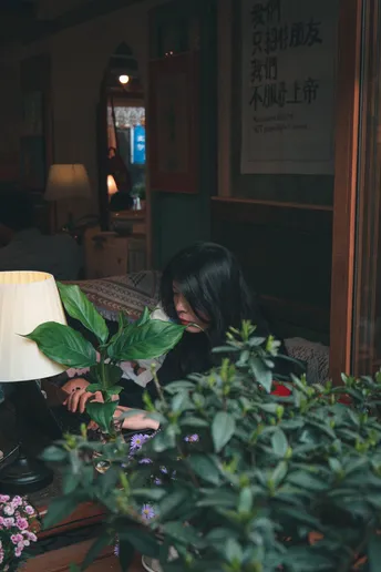 一个人坐在有灯的房间里 桌子上开着花。