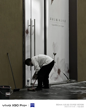 一位男士正在清洗一栋楼房旁边的白色花朵的地面。