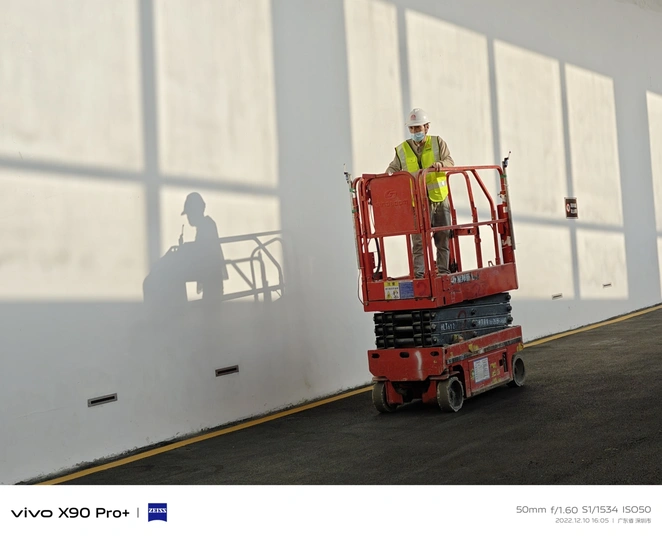 一名建筑工人站在一栋建筑内的红色起重机上 周围有大型窗户。