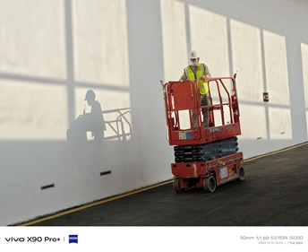 一名建筑工人站在一栋建筑内的红色起重机上 周围有大型窗户。