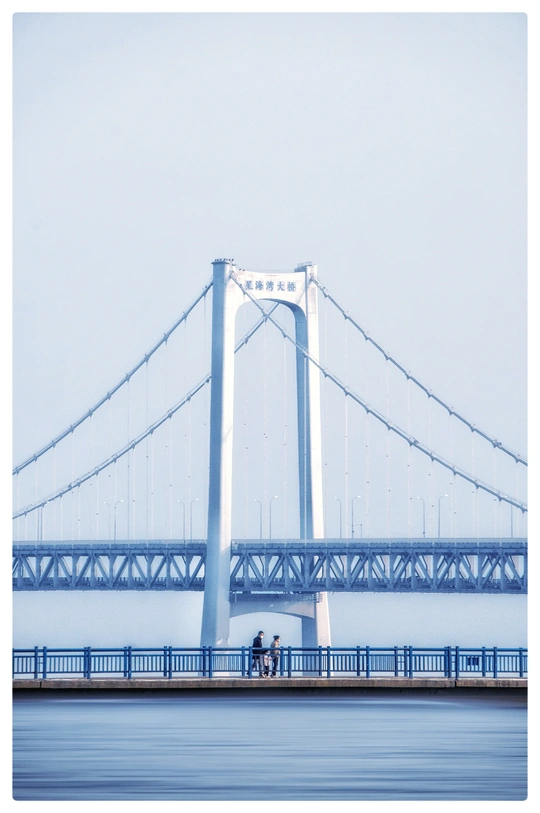 一个骑自行车的人在桥边站立 桥上有行人通过。