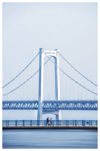 一个骑自行车的人在桥边站立 桥上有行人通过。