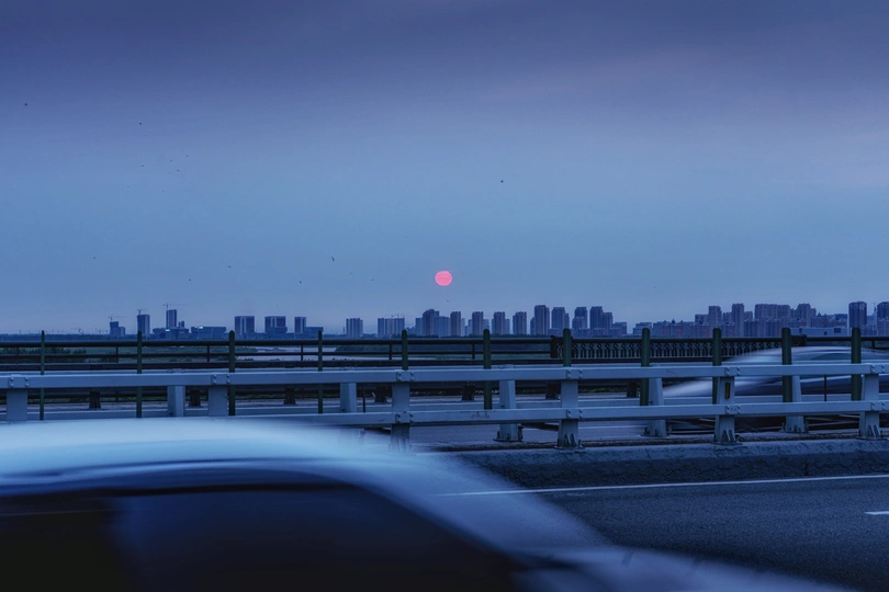 天空中的粉红色月亮在夕阳下升起 城市天际线上的汽车在黄昏时分排成一条公路。