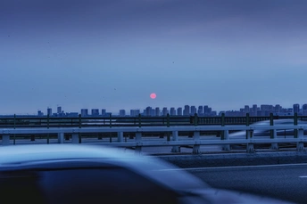 天空中的粉红色月亮在夕阳下升起 城市天际线上的汽车在黄昏时分排成一条公路。