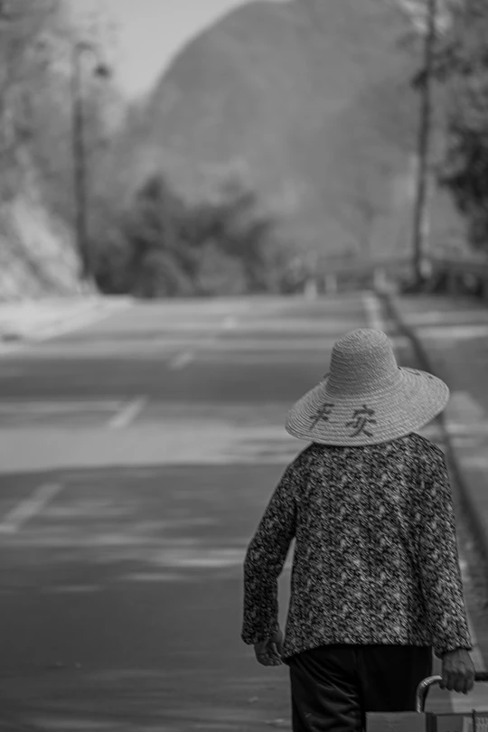 一个戴帽子 拿着行李箱的老妇人走在大街上