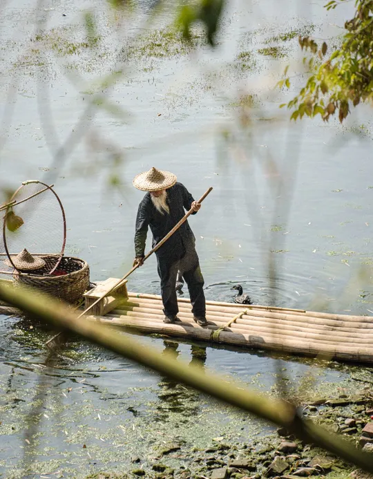 一个戴帽子的人在过河时站在一只小木筏上 带着一只篮子。
