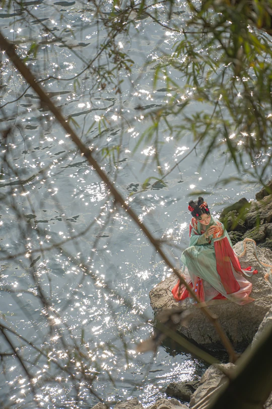 坐在水边岩石上的一尊女人雕像 旁边还有一个人坐在岩石上。