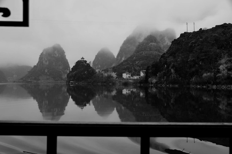 一张黑白图片 背景是山脉 前景有小船在水上。