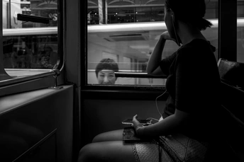 一个黑白照片 一个年轻的男孩坐在火车上 正在窗口看着一个正在玩手机的女人。