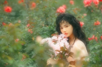 美丽的年轻女子在玫瑰花田中闻着红玫瑰的照片