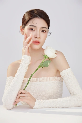 一位年轻女子手里拿着一朵白玫瑰 用一块白毛巾捂住脸
