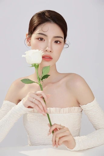 一位美丽的年轻女子举着一朵白玫瑰