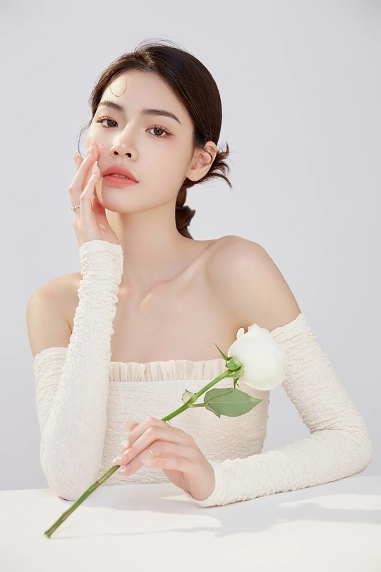 一位女子手持一朵白玫瑰花靠近她的脸