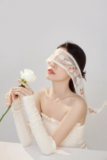 一个戴着面纱的美丽年轻女子拿着一朵白玫瑰