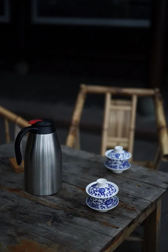 一个木制桌子 上面放着一个茶壶、一杯茶和一只蓝色的白瓷碗。