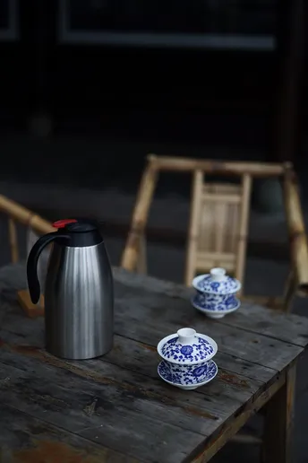 一个木制桌子 上面放着一个茶壶、一杯茶和一只蓝色的白瓷碗。