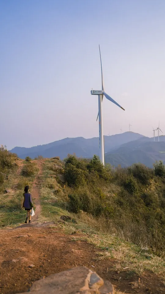 一个人和一个女人在一条小径上行走 远处可以看到一座山上的风车。