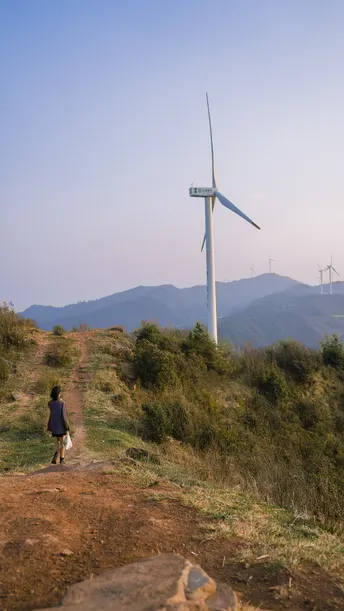 一个人和一个女人在一条小径上行走 远处可以看到一座山上的风车。