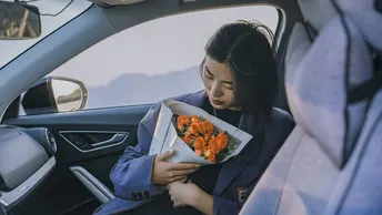 一个年轻女子坐在汽车里 手里拿着一束花。