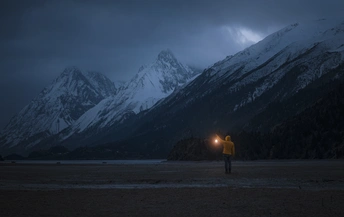在一个雪山的黑暗中站着一个拿着灯的人