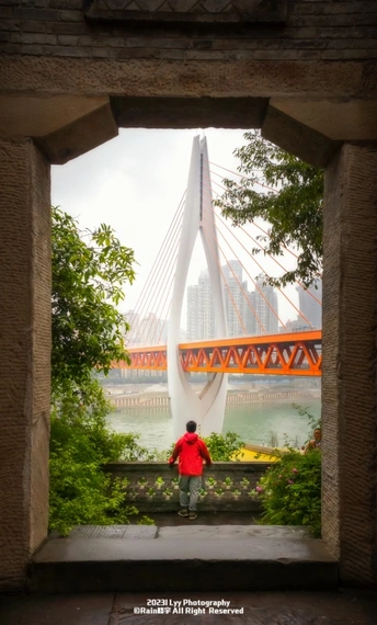 一位穿红衣服的男子站在一座河上的桥上