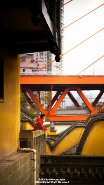 一位穿红衣服的女人站在桥上 背景中有一个男人在走。