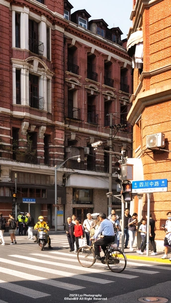 城市的一个交叉口 人们骑自行车 行人穿越街道 前方是建筑。