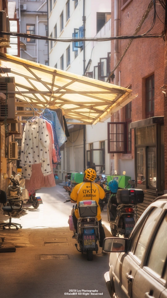 一条狭窄的巷子 停满了汽车和摩托车 停在建筑物的侧面 下面有遮阳篷。