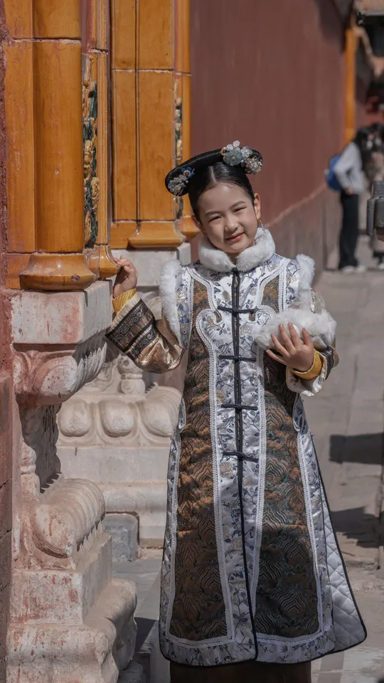 一位穿着传统服装的年轻女子站在街角一栋建筑前。