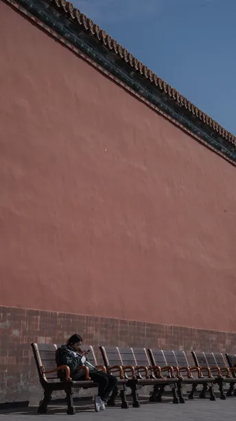 一个人坐在木凳上 前面是红色墙壁 空荡荡的椅子