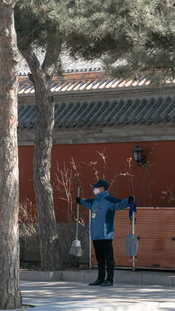 一个人穿着蓝色在公园里走 旁边有一棵树和一座建筑。