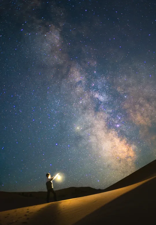 一个站在沙丘上的人 在夜晚仰望星空。